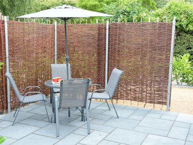 An outdoor patio with a round table and four grey chairs under a large umbrella at Bramertons Nest Long Melford