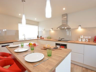 A kitchen with a wooden island countertop set with plates and green glasses and red bar stools at Bramertons Nest Long Melford