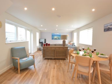 A living room and dining area with a wooden table set for four, a blue armchair, a wooden cabinet, and a sofa at Bramertons Nest Long Melford