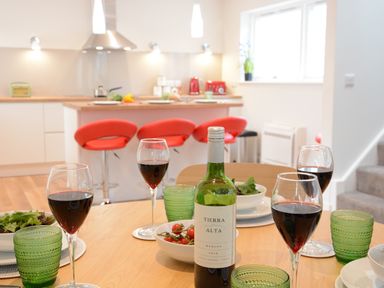 A kitchen and dining area with a table set with wine glasses and a bottle of red wine at Bramertons Nest Long Melford