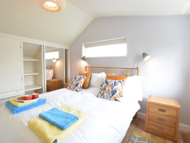 A bedroom with a double bed with pillows and towels and two wooden bedside tables with lamps at Bramertons Nest Long Melford