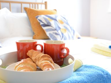 A tray with two red mugs and two croissants on a bed with colorful pillows and towels at Bramertons Nest Long Melford