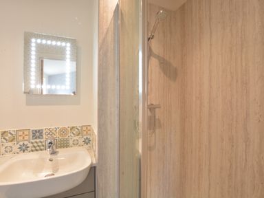 A bathroom with a sink and illuminated mirror next to a shower enclosure with a handheld shower head at Bramertons Nest Long Melford