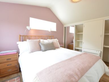 A bedroom with a double bed, pillows, bedside table with folded towels, and built-in cupboards at Bramertons Nest in Long Melford