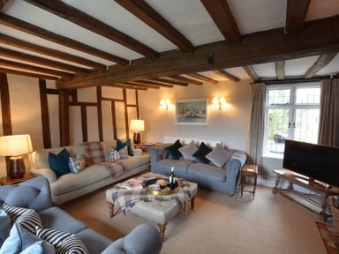 A living room with wooden ceiling beams sofas a TV and a window at Old Valley Farm in Walberswick