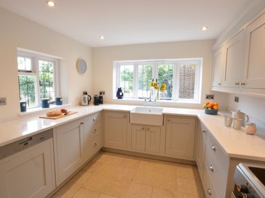 A kitchen with white cabinets a farmhouse sink under a window and various kitchen items on countertops at Old Valley Farm in Walberswick