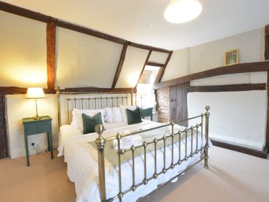 A bedroom with a metal bed frame bedside tables and lamps and exposed wooden beams at Old Valley Farm in Walberswick