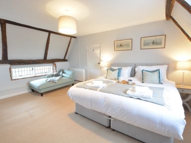 A bedroom with a large bed, two lamps, framed pictures on the wall, and a chaise lounge by a window at Old Valley Farm in Walberswick