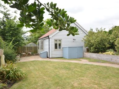 A small white wooden house with a red roof and blue storage units in a garden with a patio table and chairs at Old Valley Farm in Walberswick