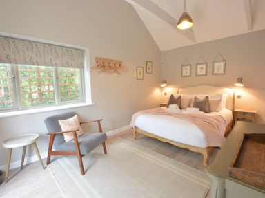 A bedroom with a bed pillows and towels a chair with a cushion a side table and framed pictures at Old Valley Farm Walberswick