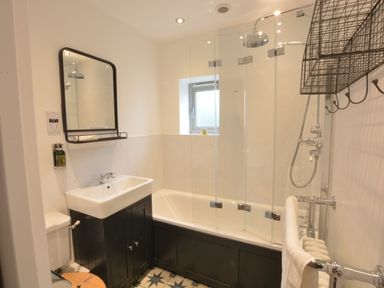 A bathroom with a bathtub shower combination a sink with a mirror above and a wall-mounted metal rack at Old Valley Farm in Walberswick