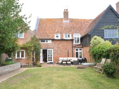 A garden with lawn chairs and outdoor seating area behind a brick house with a tiled roof at Old Valley Farm in Walberswick