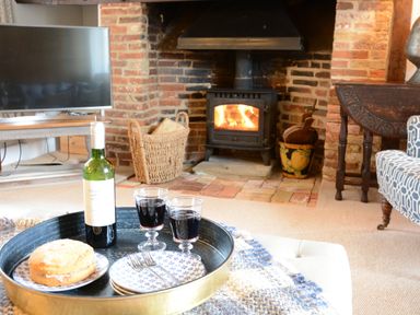A living room with a wood burning stove bottle of wine and cake on a tray at Old Valley Farm in Walberswick