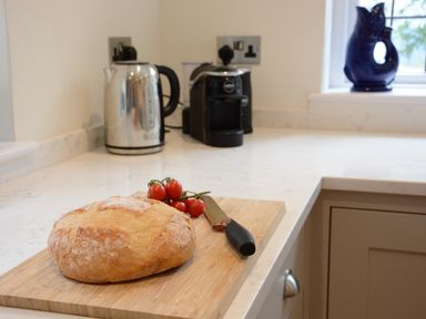 A kitchen countertop with a loaf of bread and tomatoes on a cutting board and a knife kettle and coffee machine visible at Old Valley Farm in Walberswick