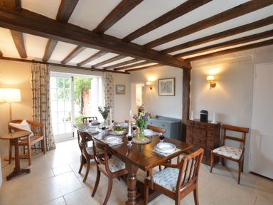 A dining room with a wooden table set for six with plates and glasses and wooden chairs with patterned cushions at Old Valley Farm Walberswick