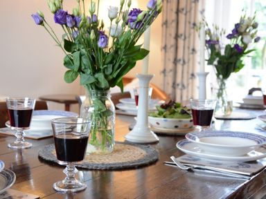 A dining table set with plates glasses of red wine flower vases and candlesticks at Old Valley Farm Walberswick