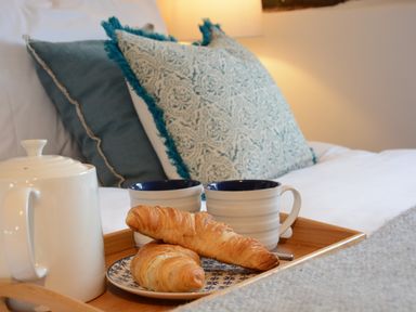 A breakfast tray with croissants teapot and mugs on a bed with pillows at Old Valley Farm Walberswick