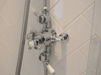 A close up of a chrome shower valve with a hose attached on white tiled wall at Old Valley Farm in Walberswick