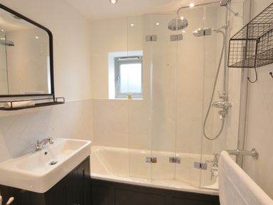 A bathroom with a sink a mirror a bathtub with a glass shower screen and a metal shelf at Old Valley Farm in Walberswick
