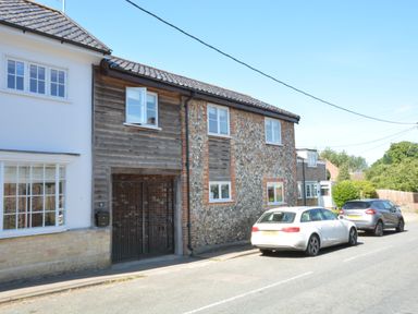 A street view with parked cars and houses with brick and wood exterior at May Barn Ixworth in Bury St Edmunds