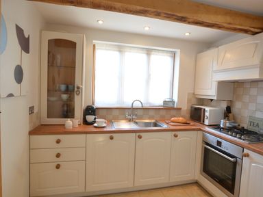 A kitchen with white cabinets wooden countertops a sink oven microwave and a window at May Barn Ixworth in Bury St Edmunds