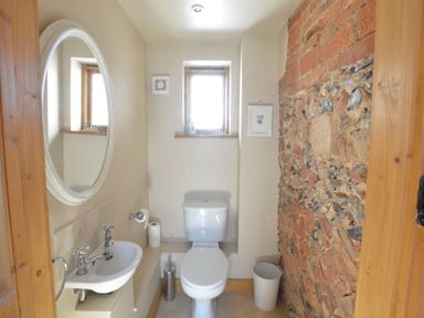 A small bathroom with a toilet a sink a round mirror a window and a brick wall at May Barn Ixworth Bury St Edmunds