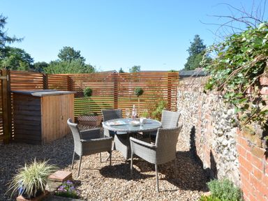 An outdoor patio area with a round table and four wicker chairs on a gravel surface at May Barn in Ixworth Bury St Edmunds