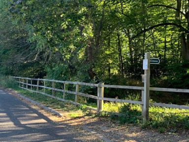 A roadside with a wooden fence and a signpost pointing to bridleway near a wooded area at May Barn Ixworth Bury St Edmunds