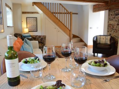 A dining table set with wine glasses and bowls of salad in a living area with sofas stairs and a chair at May Barn Ixworth Bury St Edmunds