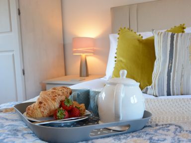 A breakfast tray with croissants strawberries a teapot and cups on a bed with pillows and a lamp at May Barn Ixworth in Bury St Edmunds
