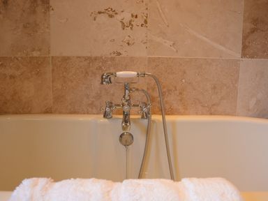 A bathtub with a silver faucet and shower attachment against a tiled wall at May Barn Ixworth in Bury St Edmunds