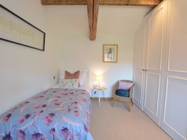 A bedroom with a single bed with floral bedding a side table with a lamp a chair with cushions and built in wardrobes at May Barn Ixworth Bury St Edmunds