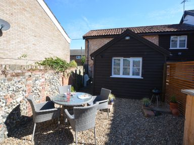 An outdoor patio with a round glass table and four chairs beside a black wooden shed at May Barn Ixworth in Bury St Edmunds