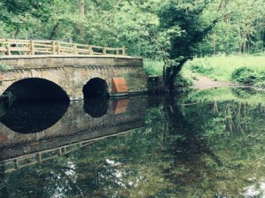 A stone bridge over a river surrounded by trees at May Barn Ixworth in Bury St Edmunds