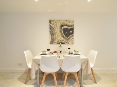 A dining room with a table set for four with white chairs and a patterned painting on the wall at The Smokehouse Cottage in Southwold