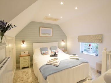 A bedroom with a double bed side tables paintings and a window at The Smokehouse Cottage in Southwold