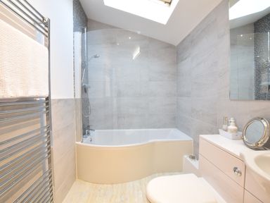 A bathroom with a bathtub shower combo towel rack and sink at The Smokehouse Cottage in Southwold