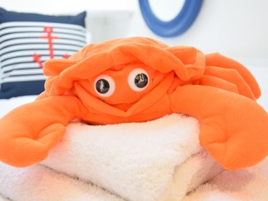 A plush orange crab toy on white towels with a pillow featuring a red anchor on striped fabric at The Smokehouse Cottage in Southwold