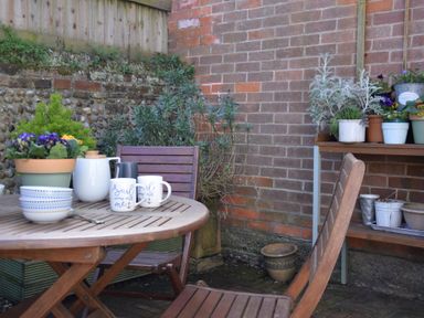 A small outdoor patio with a wooden table and chairs surrounded by potted plants at The Smokehouse Cottage in Southwold