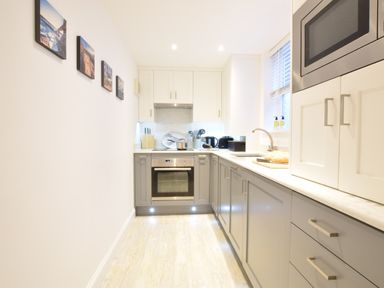 A galley kitchen with grey and white cabinets oven and microwave on wall at The Smokehouse Cottage in Southwold
