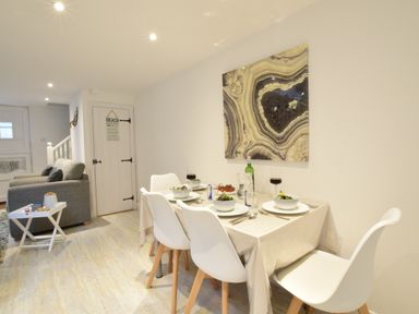 A dining table set for four with bowls and glasses next to a living area with two armchairs at The Smokehouse Cottage in Southwold