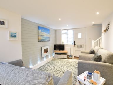 A living room with gray sofas a television on a wooden stand a wall-mounted electric fireplace and a rug at The Smokehouse Cottage in Southwold
