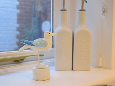 A kitchen windowsill with a wooden bird figure and ceramic oil and vinegar bottles at The Smokehouse Cottage in Southwold