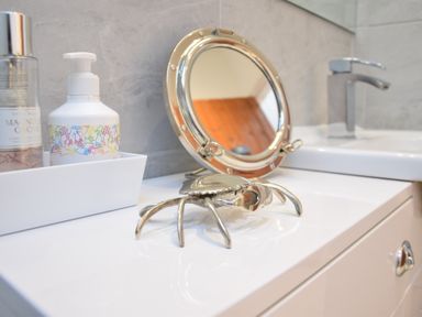 A bathroom counter with hand soap a decorative crab and a round mirror at The Smokehouse Cottage in Southwold