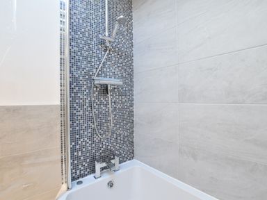 A bathroom with a bathtub shower combination with mosaic tile wall at The Smokehouse Cottage in Southwold