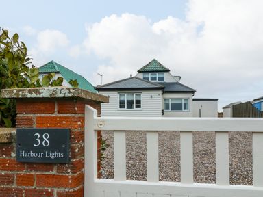 A white house with green roof tiles behind a white gate and brick pillar with a plaque reading 38 Harbour Lights in Southwold