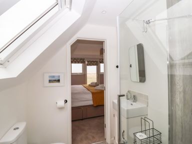 A bathroom with a toilet sink and shower visible through a doorway to a bedroom with a bed and windows at Harbour Lights Southwold