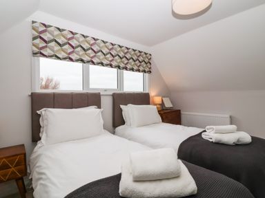 A bedroom with two single beds with white bedding and dark gray blankets at Harbour Lights in Southwold