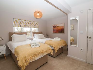 A bedroom with two single beds with yellow blankets and white linens a bedside table with a lamp a wall mirror and a painting at Harbour Lights in Southwold