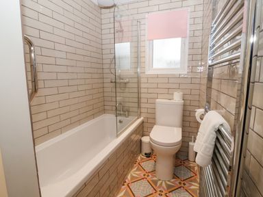 A bathroom with a bathtub a shower a toilet a small window and a towel on a heated rack at Harbour Lights in Southwold